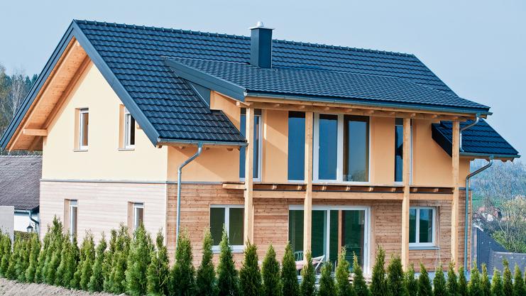 Moderne zweigeschossige Wohnhausfassade mit Holzverkleidung und großen Fenstern, umgeben von niedrigem Grün.